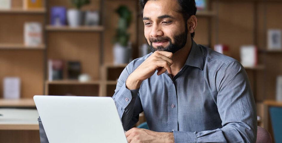 Smiling bearded real estate lawyer remote working on laptop in home office